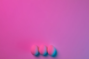 Egg hunt is coming. Easter traditions, pink-blue colored eggs on pink background, neon light, top view, copyspace for ad. Concept of holidays, spring, celebrating, food and sweets, family time.