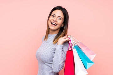 Woman over isolated pink background holding shopping bags and smiling