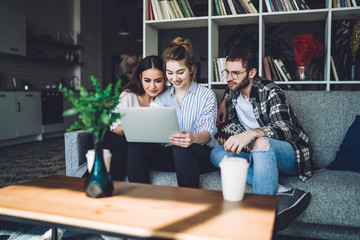 Friends sitting at couch and watching movie at laptop