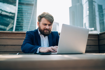 Fototapeta premium Worried businessman working on laptop in street