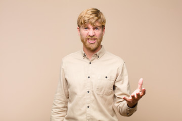 young blonde man looking angry, annoyed and frustrated screaming wtf or what’s wrong with you...