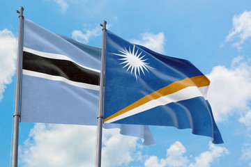 Marshall Islands and Botswana flags waving in the wind against white cloudy blue sky together. Diplomacy concept, international relations.