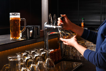 Hands of female bartender pouring from tap fresh beer into the glass in pub