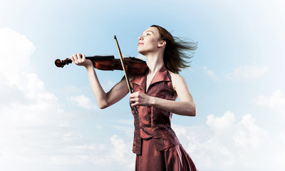 Woman violinist in red dress playing melody against cloudy sky