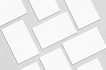 Closeup of empty white rectangle business card mockups lying diagonally on neutral grey concrete background. Flat lay, top view. Open composition. Blank Template for Corporate Identity. Copy space