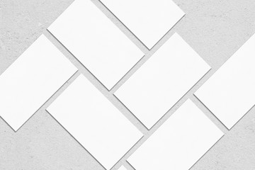 Closeup of empty white rectangle business card mockups lying diagonally on neutral grey concrete...