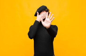 young french artist man covering face with hand and putting other hand up front to stop camera,...