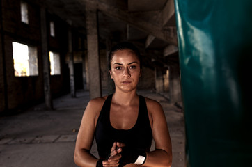Fototapeta na wymiar Portrait of female boxer next to the boxing bag in warehouse.