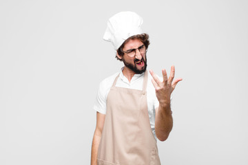 young crazy chef looking angry, annoyed and frustrated screaming wtf or what’s wrong with you...