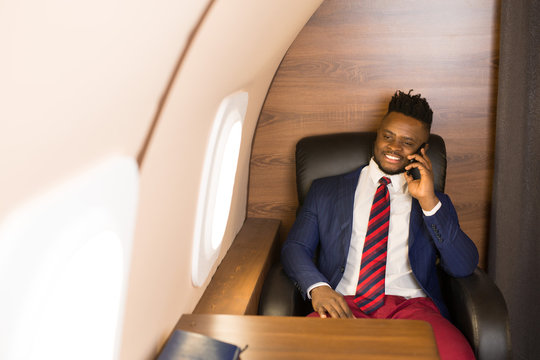 handsome african young man in a suit in the cabin of a private jet with a phone in his hand