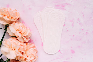 feminine hygiene products on a light background with pink flowers. flat lay of laying and flowers
