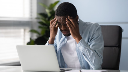 Stressed African worker touching temples feels unhealthy suffers from headache