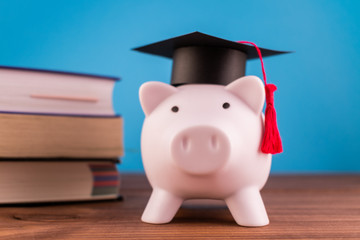 Piggy bank with a graduation hat and a lot of books on a light blue backround. Student scolarship...