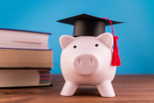 Piggy Bank With A Graduation Hat And A Lot Of Books On A Light Blue Backround. Student Scolarship Save Concept. Finance Concept.