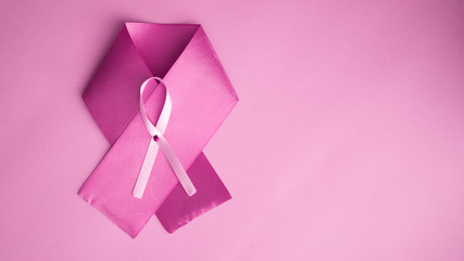 Pink satin breast cancer awareness ribbon on pink background.