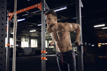 Fototapeta na wymiar Young healthy man, athlete doing exercises, pull-ups in gym. Single male model practicing hard and training his upper body. Concept of healthy lifestyle, sport, fitness, bodybuilding, wellbeing.