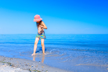Child girl in summer straw hat is dancing happy barefoot in shallow sea water, beach