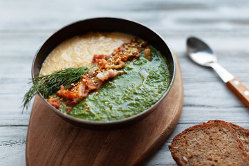 Spinach and corn soup puree in a bowl with grilled meat and spinach leaves on white wooden background, top view