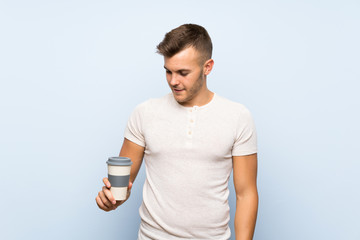 Young handsome blonde man over isolated blue background holding hot cup of coffee