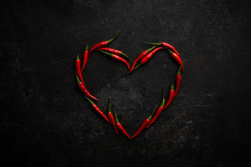 Spicy red chili pepper in the shape of a heart on a dark stone background, design concept for...
