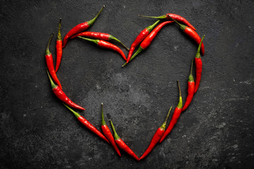 Spicy red chili pepper in the shape of a heart on a dark stone background, design concept for...
