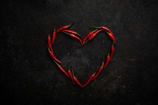 Spicy red chili pepper in the shape of a heart on a dark stone background, design concept for Valentine's day