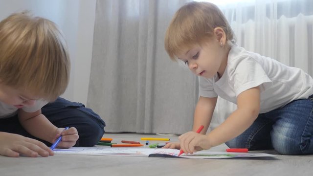 children draw with felt-tip pens in an album. little boy and girl concept childhood brother and sister play paint on floor with colored markers lifestyle