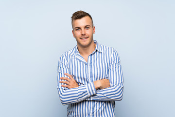 Young handsome blonde man over isolated blue background keeping the arms crossed in frontal position