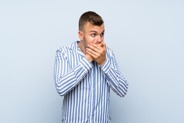 Young handsome blonde man over isolated blue background covering mouth and looking to the side