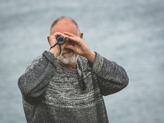 Senior man looking through the binoculars against sea background.