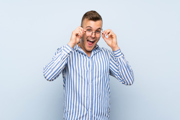 Fototapeta premium Young handsome blonde man over isolated blue background with glasses and surprised
