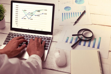 Desk, white table with a computer, a graph, and a magnifying glass and notebook.
