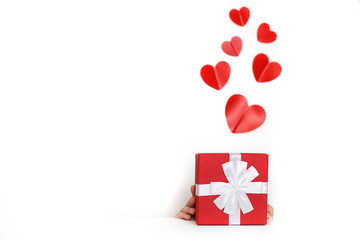 a young man holding a present box with red hearts on a white background. child covers his face with a box
