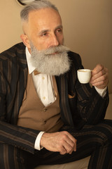 Senior handsome concentrated man with beard in business suit sitting and drinking coffee.