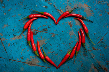 Hot red chili pepper in the shape of a heart on a blue wooden table, design concept for Valentine's...