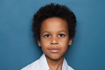 Clever black child student boy looking at camera on blue background, close up portrait