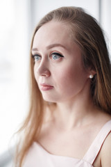 Close-up portrait of natural candid good-looking woman with gray eyes and long hair, looking out the window