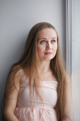 Portrait of young attractive female with beautiful long hair sitting near window looking out and smiling