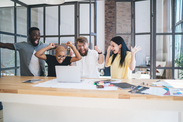 Group of enthusiastic multiethnic coworkers using laptop at office