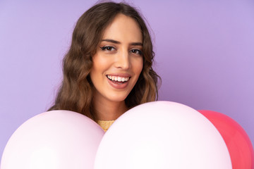 Young woman catching many balloons over isolated on purple background