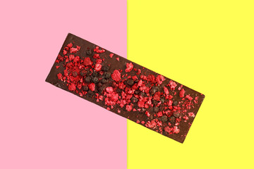 Dark chocolate bar with dried red berries on bright pink and yellow background