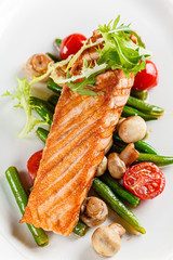 European cuisine. A large steak of red salmon fish, with mushrooms, asparagus, cherry tomatoes and fried lemon. Serving dishes in a restaurant on a white plate.