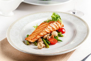 European cuisine. A large steak of red salmon fish, with mushrooms, asparagus, cherry tomatoes and fried lemon. Serving dishes in a restaurant on a white plate.