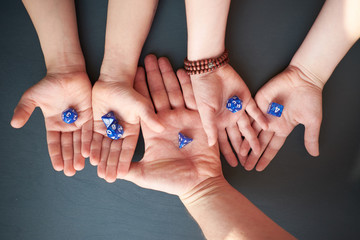 Hand of father and kids, holding role playing dices, view from above, gray background
