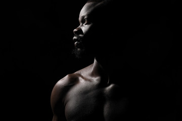portrait of a handsome black man with naked sports torso looking in the left on dark background - 320551071