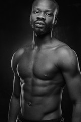 Obraz na płótnie Canvas black and white portrait of a handsome black man with naked sports torso looking in the camera on dark background