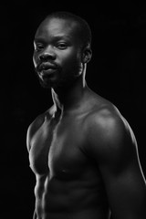 Fototapeta premium black and white portrait of a handsome black man with naked sports torso looking in the camera on dark background
