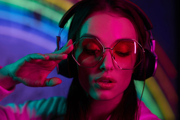 colored portrait of a beautiful young girl in neon light  she has glasses and headphones she looks away - 320553225