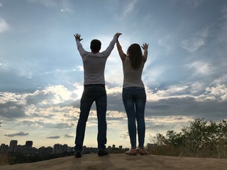 A man and a girl raise their hands to the sky. Two lovers stand together and look into the distance.
