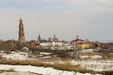  116 / 10000 АНГЛИЙСКИЙ Перевести вGoogleBing View from a distance of the Church ensemble standing on a hill with a high red brick bell tower and colored buildings